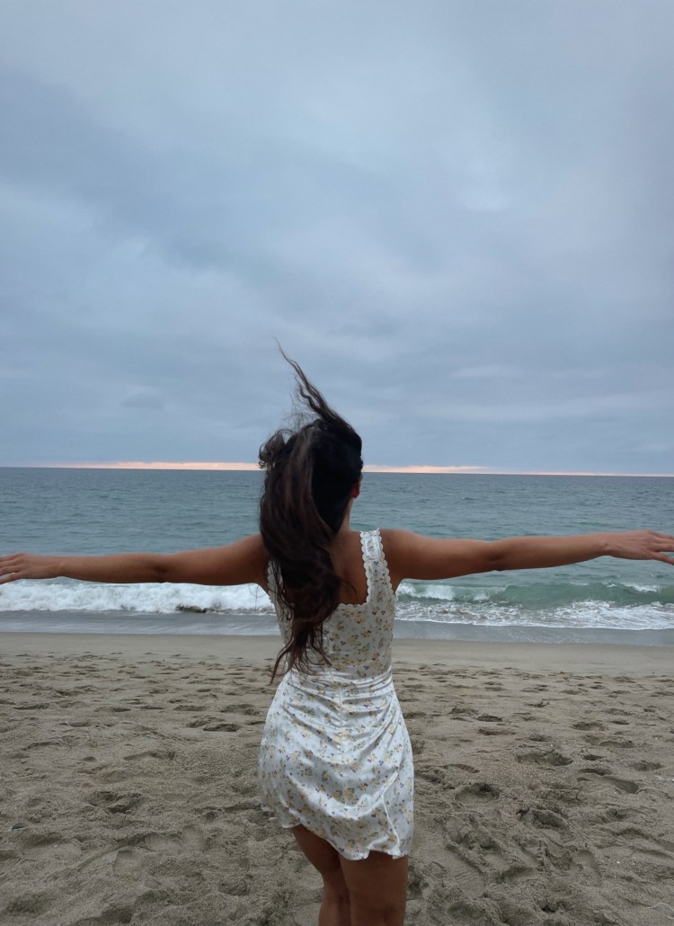 woman running into the sunset wearing a white silk floral dress in malibu california for a flower garden beach picnic